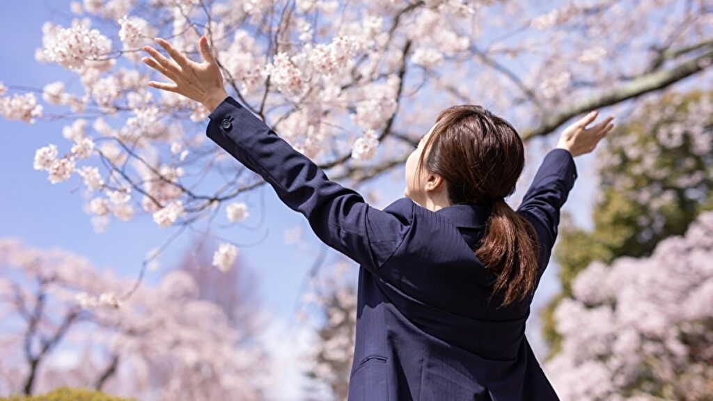 桜の木の下で両手を広げて喜ぶ女性